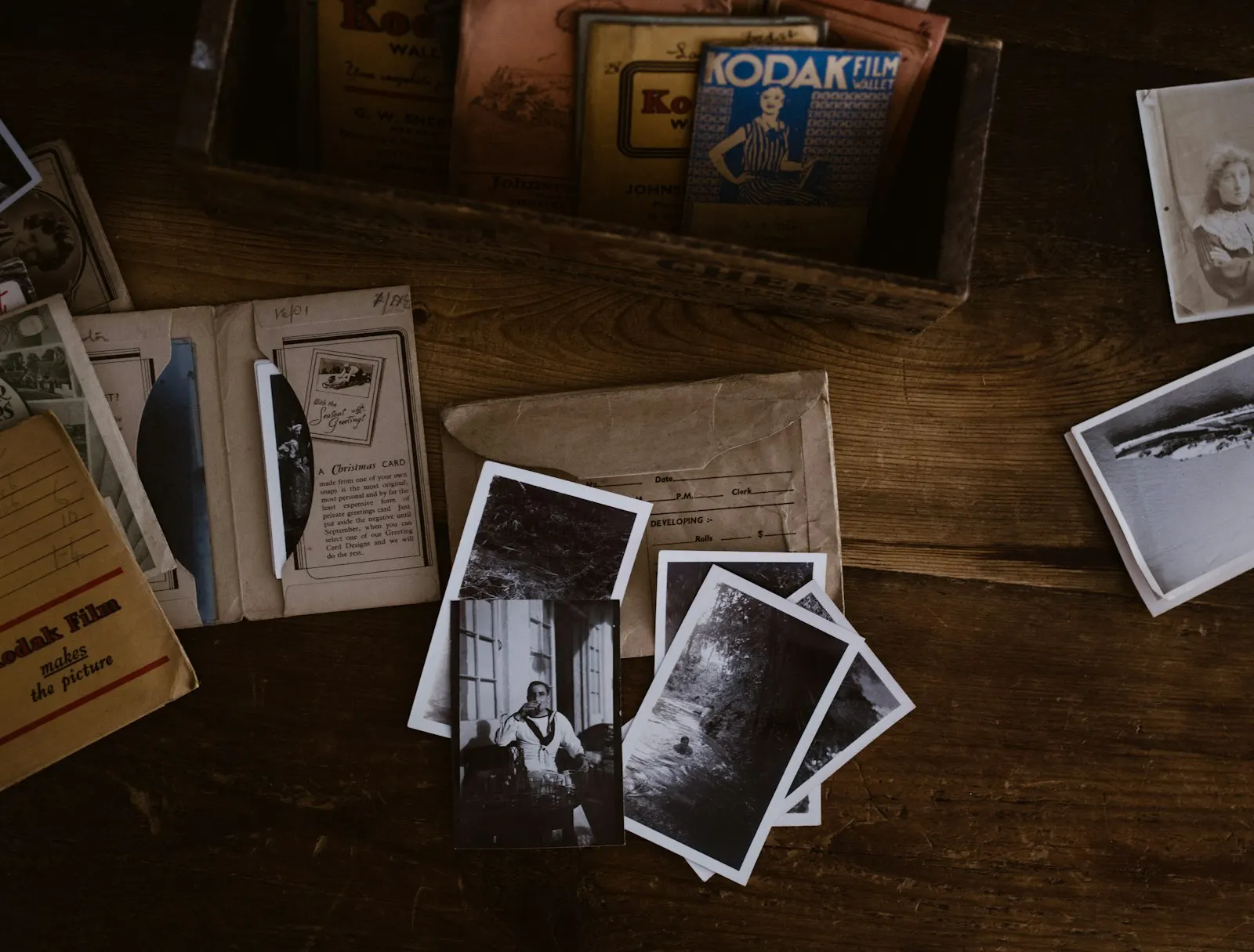 Photographies anciennes et pochettes de tirages posées sur une table en bois, souvenirs de famille